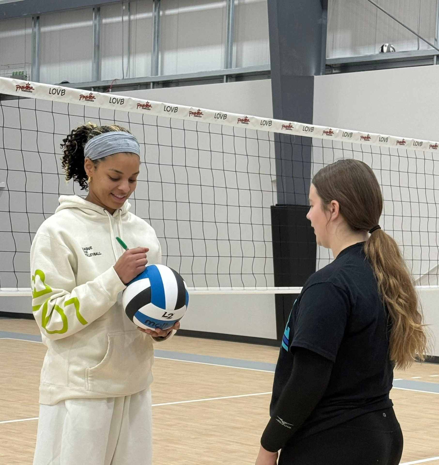 Alexis Hart signing a volleyball for a young player next to the net